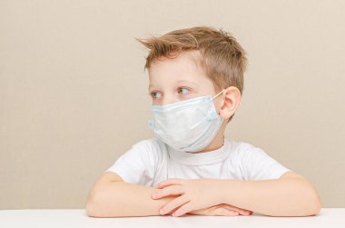 Tıbbi maske takan dört yaşında tatlı bir çocuk. Salgın yüzünden karantinaya alınmış çocuklar. Çocuk evde üzgün ve yalnız oturuyor.