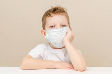 Tıbbi maske takan dört yaşında tatlı bir çocuk. Salgın yüzünden karantinaya alınmış çocuklar. Çocuk evde üzgün ve yalnız oturuyor.