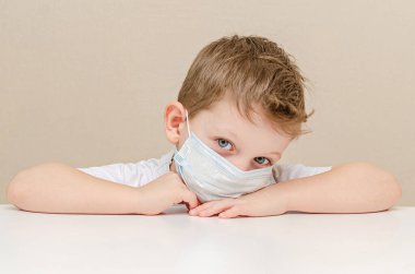 Tıbbi maske takan dört yaşında tatlı bir çocuk. Salgın yüzünden karantinaya alınmış çocuklar. Çocuk evde üzgün ve yalnız oturuyor.