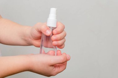 Gri arka planda dezenfektanlı bir şişeyi tutan dört yaşında bir çocuğun elleri. Sağlık önlemleri - el dezenfeksiyonu.