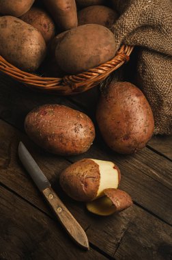 Basket with potatoes on a wooden table. Rural still life - peeling with a knife (cooking) potatoes. Rustic ordinary traditional food. clipart