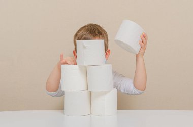 Koruyucu tıbbi maske takan dört yaşındaki sevimli çocuk tuvalet kağıdıyla oynuyor ve bir kule inşa ediyor. Çocuklarla ev karantinası, aile eğlencesi. Panovirüs (salgın) panovirüs (Covid-19) paniği