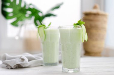 Salatalık ve bitkilerle mayalanmış süt içeceği. Işıl ışıl bir masada böyle bir kokteyl içen iki kişi. Sıcak bir yaz için ferahlatıcı bir içecek.