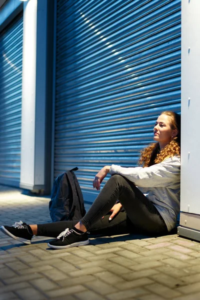 Женщина-хипстер сидит на земле возле гаражной двери . Стоковое Изображение