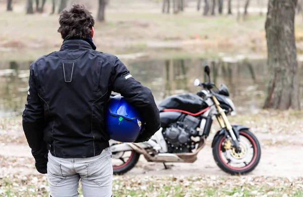 Байкер, що стоїть біля мотоцикла, тримає блакитний шолом . — стокове фото