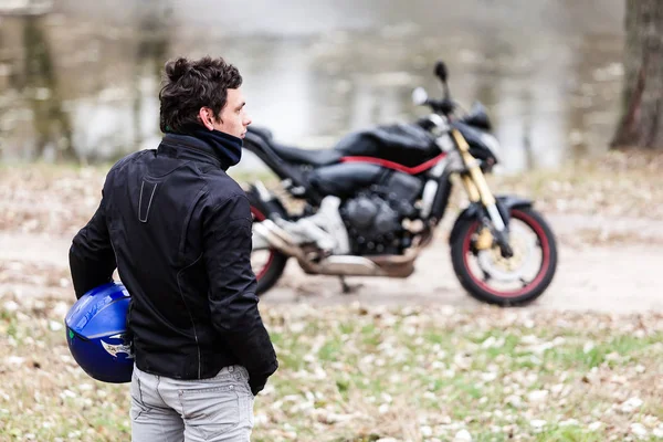 Motociclista de pé perto de moto segurando seu capacete azul . — Fotografia de Stock