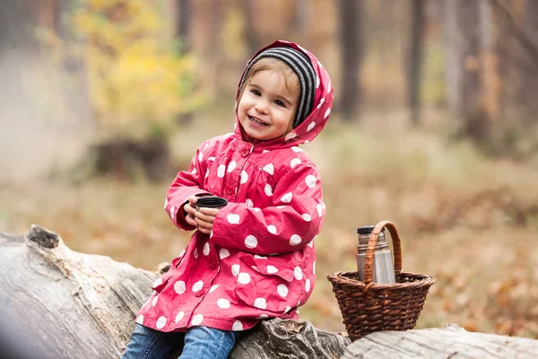 Ragazzina in giacca di pisello seduta su un albero e che beve tè . — Foto Stock