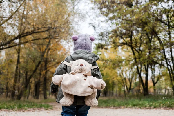 Klein meisje in de herfst bos met teddybeer rugzak. — Stockfoto