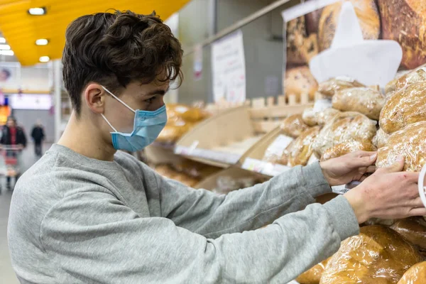 Koronavirüs salgını sırasında süpermarkette tek kullanımlık tıbbi maske takan genç bir adam. Salgın sırasında tedbirleri korumak ve önlemek. Covid-19 kişisi