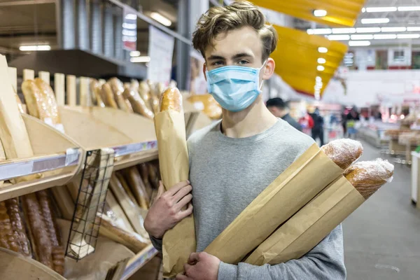 Koronavirüs salgını sırasında süpermarkette tek kullanımlık tıbbi maske takan genç bir adam. Salgın sırasında tedbirleri korumak ve önlemek. Covid-19 kişisi