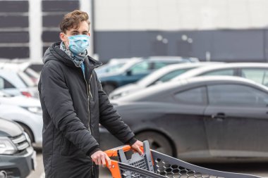 Yüz maskesi takan genç bir adam, koronavirüsten korunuyor. Covid-19 kişisi. Süpermarketin yanındaki büyük otoparkta, Corona virüsünün ortasında duruyoruz.