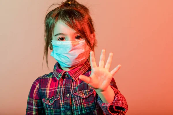 小さな女の子は 安全のために彼女の鼻の上にマスクとコロナウイルスCovid 子供から身を守るファブリックマスクを持っています スタジオは異なる色の光で撮影し ウイルスを止める — ストック写真