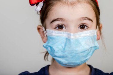 Küçük kızın kumaş maskesi var. Kendini Coronavirus COVID-19 'dan koruyor. Burnunda maske takmış bir çocuk.