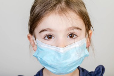 Küçük kızın kumaş maskesi var. Kendini Coronavirus COVID-19 'dan koruyor. Burnunda maske takmış bir çocuk.