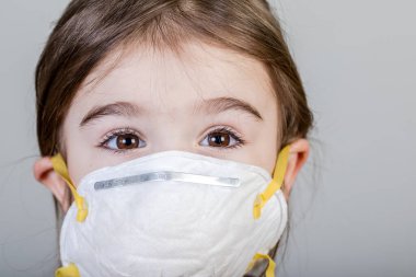 Küçük kızın kumaş maskesi var. Kendini Coronavirus COVID-19 'dan koruyor. Burnunda maske takmış bir çocuk.