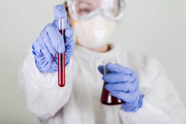 Korumalı giysideki doktor Coronavirus COVID-19 analizi için kanla test tüpü tutuyor. Grip aşısı, koronavirüs, ebola..