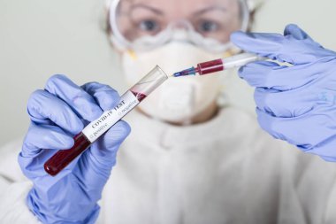 Korumalı giysideki doktor Coronavirus COVID-19 analizi için kanla test tüpü tutuyor. Grip aşısı, koronavirüs, ebola..