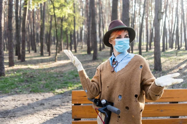 コロナウイルスから身を守るためにマスクと手袋をしたスタイリッシュな女性 都市や公園内の電動スクーターを使用して安全になるために — ストック写真