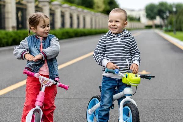 Kids riding bikes in a park. Children enjoy bike ride in the city. Brother and sister friends forever. Girl with pink bike and a boy with blue one.
