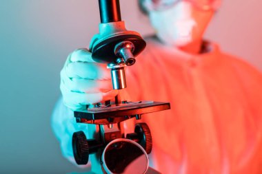 Coronavirus COVID-19 analizi için mikroskop tutan koruyucu giysili bir doktor. Grip aşısı, koronavirüs, ebola..