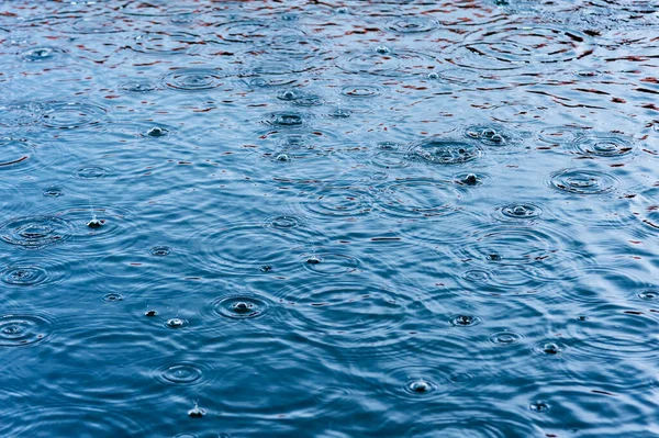 水坑中的水面上的雨滴 带有深浅的黑色阴影和蓝天的反光 — 图库照片