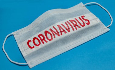 Mavi arka planda Coronavirus yazılı tıbbi yüz maskesi. Koronavirüs karantinası kavramı.