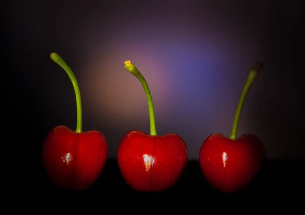 A sötét háttér előtt három cseresznye — Stock Fotó