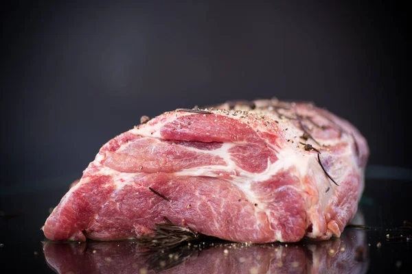 Carne crua de parte de porco com temperos e alecrim em um escuro — Fotografia de Stock