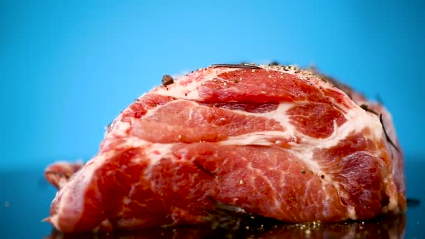 Trozo de carne de cerdo carne cruda con especias y romero en un azul — Vídeos de Stock