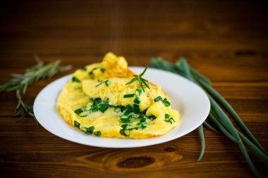 Tahta bir tabakta doğranmış yeşil soğanlı kızarmış omlet.