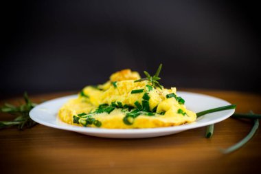 Tahta bir tabakta doğranmış yeşil soğanlı kızarmış omlet.