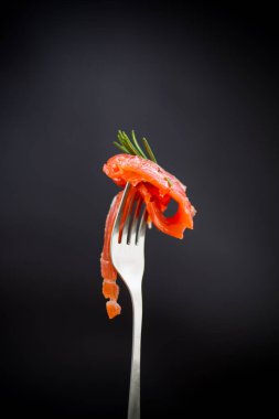 Çatallı, siyah arka planda tuzlu kırmızı balık dilimi.