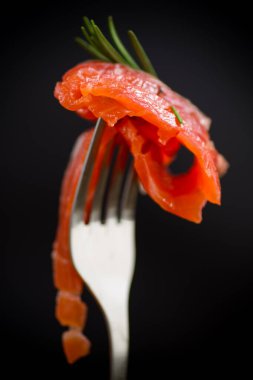 Çatallı, siyah arka planda tuzlu kırmızı balık dilimi.