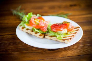 Salata yapraklı kızarmış ekmek ve ahşap bir masada tuzlanmış kırmızı balık.