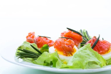 Beyaz arka planda tuzlanmış kırmızı balıklı haşlanmış yumurta ve salata yaprakları.