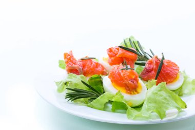 Beyaz arka planda tuzlanmış kırmızı balıklı haşlanmış yumurta ve salata yaprakları.