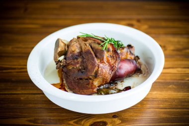 Ahşap bir masada, seramik formda baharatlı fırında domuz inciği.