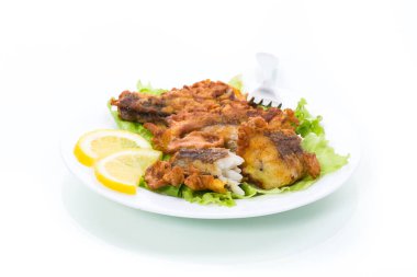 Kızarmış hake balığı, marul ve limonla birlikte beyaz arka planda izole edilmiş bir tabakta.