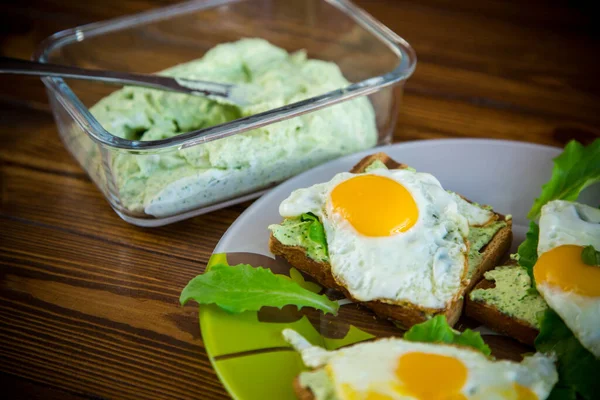 fried toast with cheese spread of arugula and fried egg in a plate on a wooden table