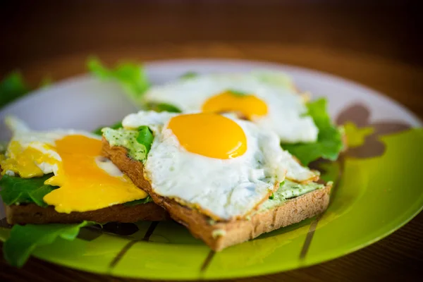 fried toast with cheese spread of arugula and fried egg in a plate on a wooden table