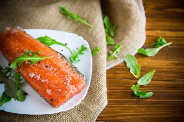Farklı baharatları olan tuzlu kırmızı balık ve ahşap bir masada bir tabakta otlar.