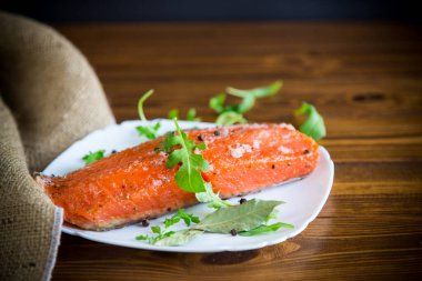 Farklı baharatları olan tuzlu kırmızı balık ve ahşap bir masada bir tabakta otlar.
