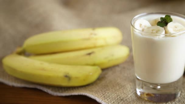 Smakelijke zelfgemaakte yoghurt met bananen in een glas op een houten tafel — Stockvideo