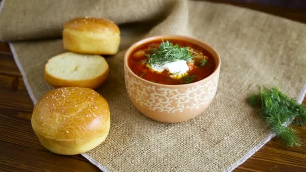 Hot beetroot soup with sour cream, herbs and rolls in a ceramic bowl — Stock Video