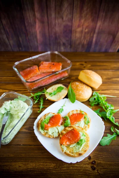 夹着炸面包 芝士和红鱼的三明治放在木制桌子上的盘子里 — 图库照片
