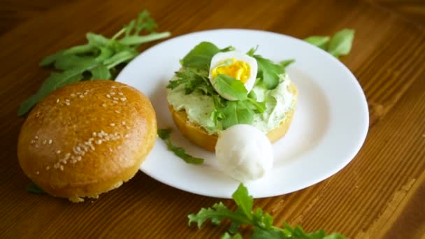 Homemade bun with cheese spread, fresh arugula and boiled egg in a plate — Stock Video