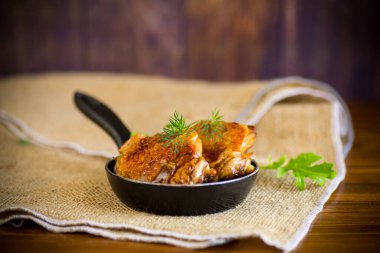 Tavuğun bacakları tavada kızarır, ahşap bir masada.
