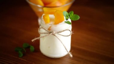 Ahşap bir masada cam kavanozdaki şeftali dilimli ev yapımı tatlı yoğurt.