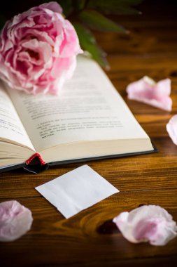 Şakayık pembe çiçek, kitap, ahşap bir masanın üzerindeki boş kart.