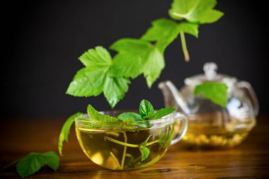 Yaz mevsiminin ferahlatıcı organik çayı, ahşap bir masanın üzerindeki cam çaydanlıkta üzümlü yapraklardan elde edilir.